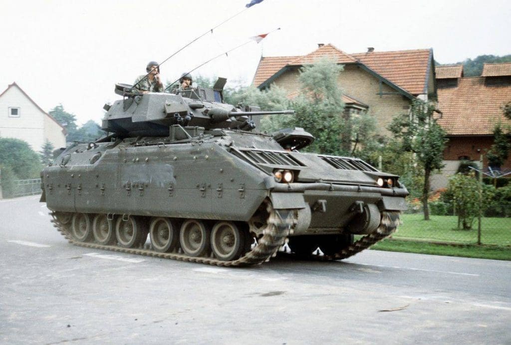 Un Vehículo de combate de caballería M-3A1 Bradley avanza por las cales de un pueblo alemán durante el ejercicio REFORGER 1985. Una de las características distinguibles de la versión de caballería del Bradley son sus troneras anuladas. Imagen: US Army.