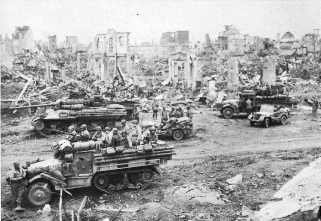 Un claro ejemplo de los medios pertenecientes a una división blindada: Jeeps, camiones y semi-orugas M-3A1 junto a un caza tanques M-36 disponen de una pausa junto a las ruinas de la ciudad de Dueren, Alemania.